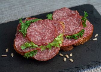 sliced ​​salami and lettuce on black background, top view. open sandwiches with sliced ​​salami sausage on rye bread