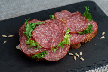 sliced ​​salami and lettuce on black background, top view. open sandwiches with sliced ​​salami sausage on rye bread