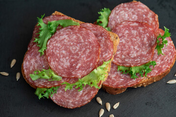 sliced ​​salami and lettuce on black background, top view. open sandwiches with sliced ​​salami sausage on rye bread