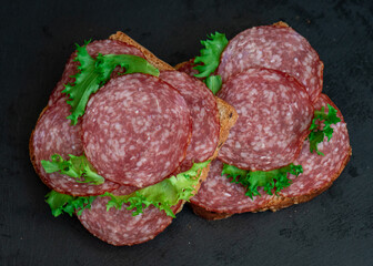 sliced ​​salami and lettuce on black background, top view. open sandwiches with sliced ​​salami sausage on rye bread