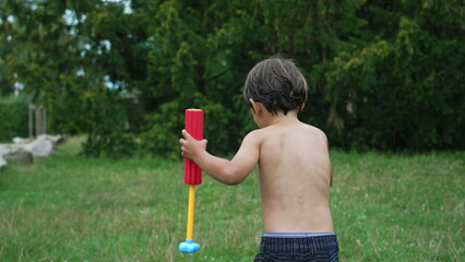 Back of child running outside in garden during summer day playing with kids water fight with toy...