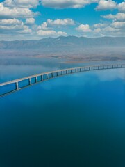 Vertical aerial view of the Lake Polyfytos Bridge with a cloudy blue sky in the background, Greece
