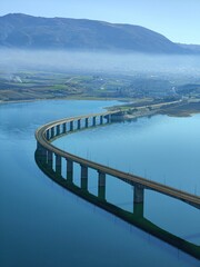 Vertical aerial view of the Lake Polyfytos Bridge with a blue sky in the background, Greece