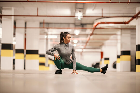 A flexible sportswoman is stretching her leg in underground garage.