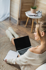 charming woman in sweater and socks using laptop in modern apartment.