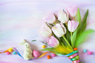 Colorful watercolor paper background with a bouquet of tulips, ribbon, bunny, candies, place for text congratulations on the Easter holiday.