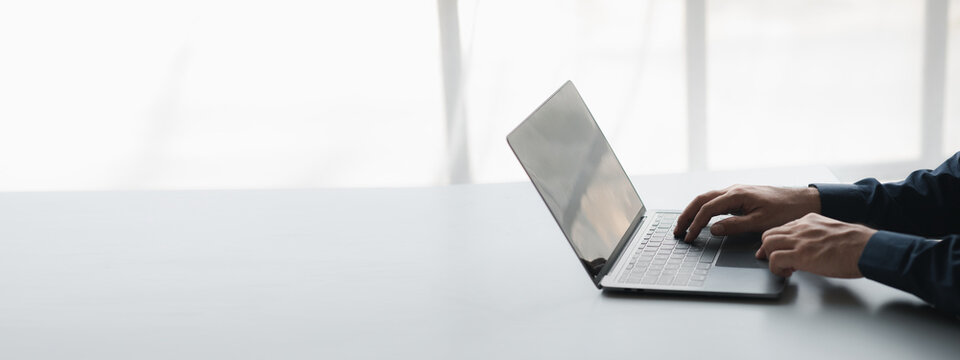 Person typing on a laptop keyboard, businessman is working in a startup company's office, he is typing messages to his colleagues and making financial documents summarizing the meetings. Copy space.