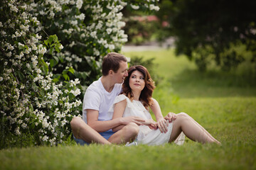 Young man and woman couple in a blooming garden near jasmine bush. Tender holding each other. Spring lovestory. Brown-haired girl with long hairs with her boyfriend or husband. Young couple on a date