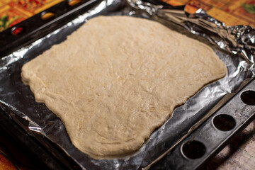 Raw dough rolled out on baking sheet. Base for pie or pizza. Uneven piece of dough at home.