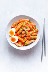 Tteokbokki with eggs, fresh green leek and  roasted sesame seeds in blue  bowl on the white  table top. Tteok-bokki is a   Korean cuisine dish with rice gnocchi sticks and spacy sauce.  Asian food