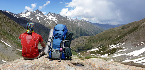 Back view of a backpacker walking alone in the Kaçkar Mountains. The man sits towards the valley and watches the mountain peaks.