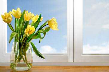 Bouquet of yellow tulips on wooden window sill on blue sky background. Springtime concept