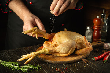 The chef salts raw chicken in a restaurant kitchen. Cooking cockerel with fragrant spices and...