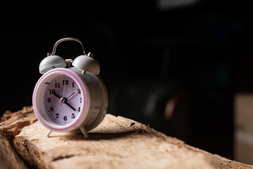 Naklejka premium Alarm clock on log on dark background. Concept of time management. Circadian rhythms.