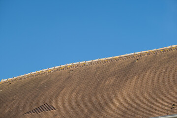 Old roof of tiles against blue sky. Roof of rural house in France.