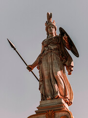 Obraz premium Statue of Athena, the ancient Greek goddess of wisdom and knowledge, who is represented as a powerful warrior with helmet, shield and spear. Travel to Athens, Greece.