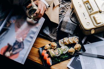 A dark-skinned African American business lady eats fresh sushi and drinks wine.