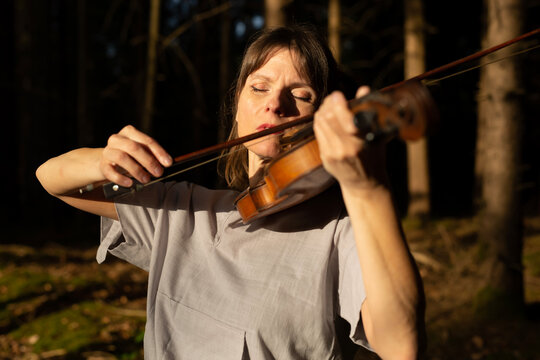 Pretty woman is simply dressed in nature in forest playing violin