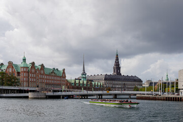 Fototapeta premium Outdoor top view over canal and tour boat and background of Børsen, waterfront building with a striking spire and Christiansborg Palace. 