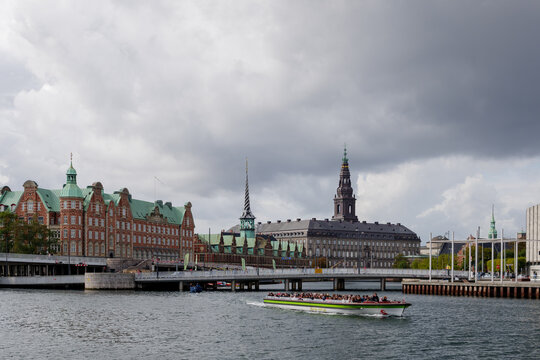 Outdoor top view over canal and tour boat and background of B&oslash;rsen, waterfront building with a striking spire and Christiansborg Palace. 