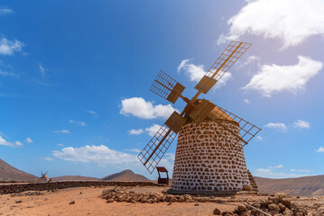 Antiguo molino de viento de ladrillo con palas de madera con el sol brillando en medio de un paisaje desértico en Fuerteventura con un cielo azul durante la puesta de sol. Recursos turísticos