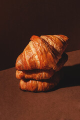 Three large golden croissants on a brown background with a side view. Stylish concept of pastries and desserts.