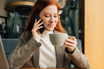 Redhead woman talking on mobile phone while drinking coffee