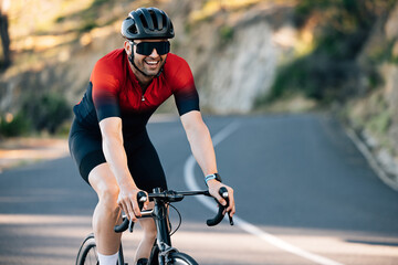 Young male cyclist smiling while riding a road bike on a hill - obrazy, fototapety, plakaty