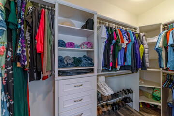 Built-in wall-mounted shelving unit in a small walk-in closet. There are rolled clothes on the shelves in between the hanging clothes on the sides.