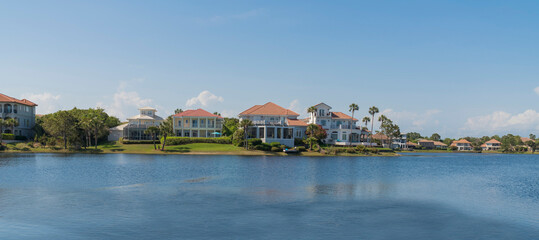Panorama of a wealthy neighborhood near Four Prong Lake in Destin, Florida. Facade of villas mansions with palm trees outdoors and views of its lakefront.