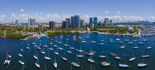 White boats on their slips at Dinner Key Marina and Coconut Grove Sailing Club. Aerial view of the beautiful ocean with anchored boats and city skyline in Miami, Florida.