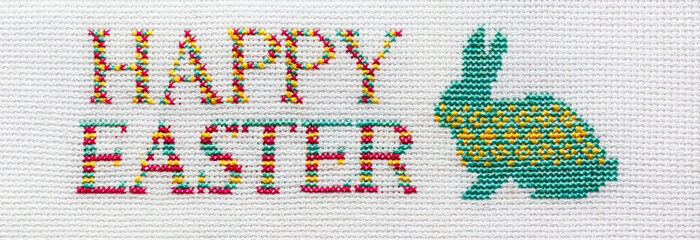 The inscription Happy Easter is embroidered with colored threads on a white fabric.