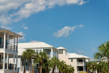 Fototapeta na wymiar Row of houses in Destin, Florida with balconies and palm trees outdoors. Houses exterior with painted light colors against the sky with clouds.