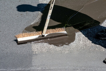 Spreading asphalt driveway sealer blending into dried asphalt on the driveway