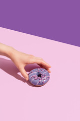 A hand with a tasty donut on a color background