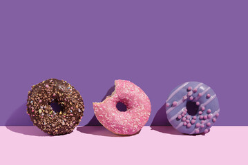 Various colorful glazed doughnuts with sprinkles on a pink background