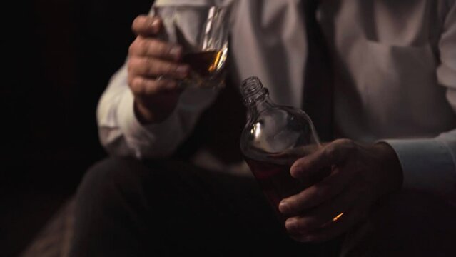 A man in a suit and tie sits at home in a hotel room and pours alcohol. Businessman drinks whiskey, scotch after a hard day, exhausted, camera moves up