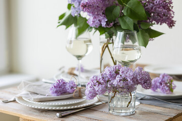 Beautiful table decor for a wedding dinner with a spring blooming lilac flowers. Celebration of a special holiday marriage event. Fancy white plates, wineglasses. Countryside style
