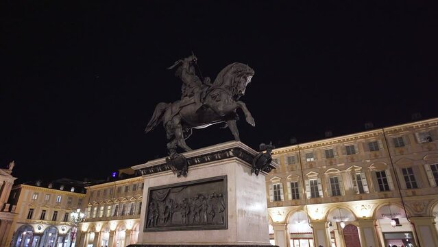 Motion shot of a statue of a horse in a square at night. Historic equestrian monument in the city of turin at night in italy. Illuminated streets in the evening, empty and bright square