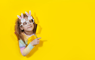 Cute  child girl in bunny shape glasses looking, peeping through the yellow paper hole. Advertise...