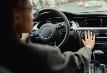 Female driver is controlling car air conditioning system grid panel on console while driving in city