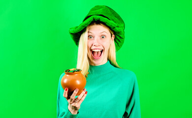 Saint Patricks Day. Happy girl in green hat with pot of gold. Smiling woman in green hat with clover holding pot of money. Tradition of Patrick Day. Female in Leprechaun hat with pot of gold coins.