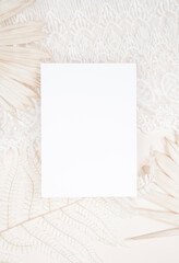 Flat lay with a blank stationery card on a boho background with dried sun palm leaves an lace