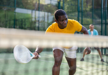 African-american male padel tennis player training on court. Man using racket to hit ball.