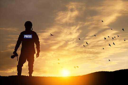 Photojournalist silhouette documenting war or conflict. Photojournalist at sunset.