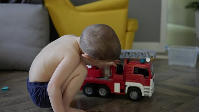 kid boy child playing toy fire truck car at home living room. little boy pretending being fireman play extinguish the fire imagine himself save life. children activity creative games indoors