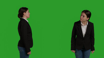 Stylish businesswoman wearing formal suit in studio, standing and waiting over greenscreen backdrop. Office employee posing on camera and smiling, acting positive over background.