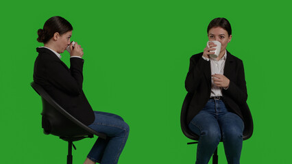 Close up of company worker serving coffee mug on camera, drinking caffeine refreshment and sitting on chair in studio. Businesswoman enjoying beverage and drink wearing formal office suit.