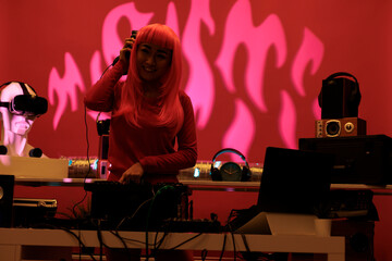 Asian woman with pink hair mixing techno music on turntables while playing record mix sounds in...