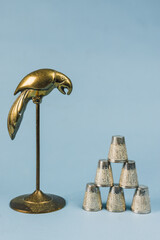 still life: brass parrot bird figure and stacked pyramid of middle eastern metal tea cups against light blue background